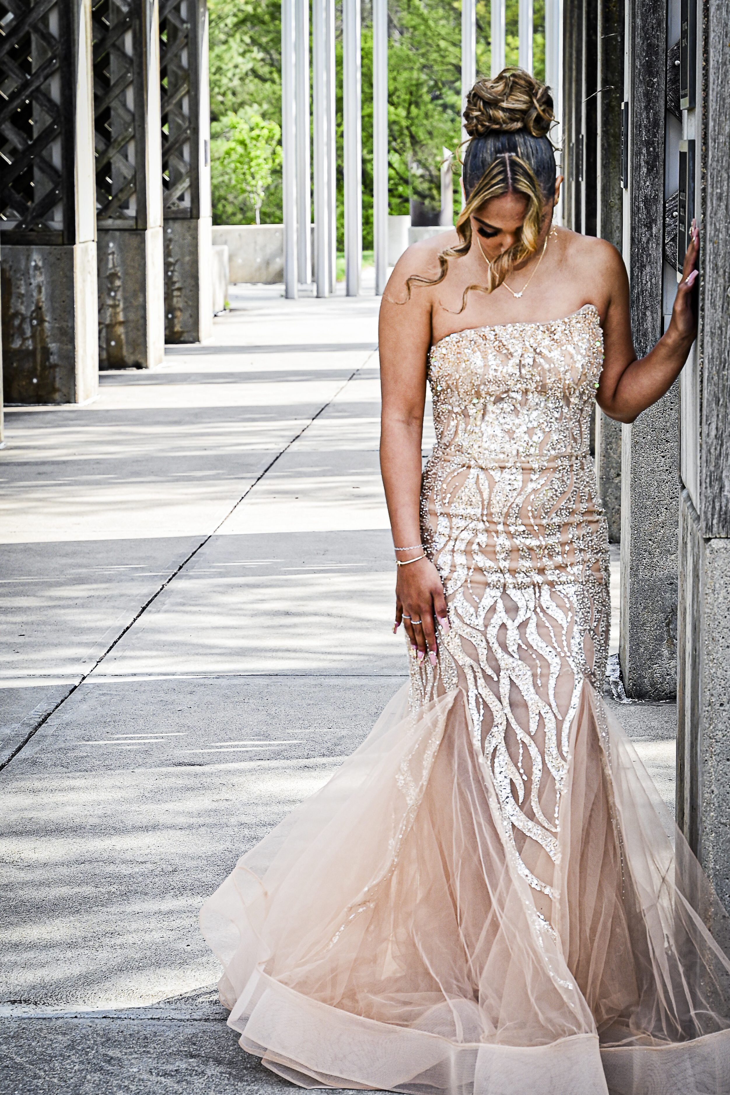 TAG_1748 Young woman in an elegant strapless sequined gown standing outdoors by a textured wall, captured in a fine art style that highlights timeless beauty and quiet, intimate moments.